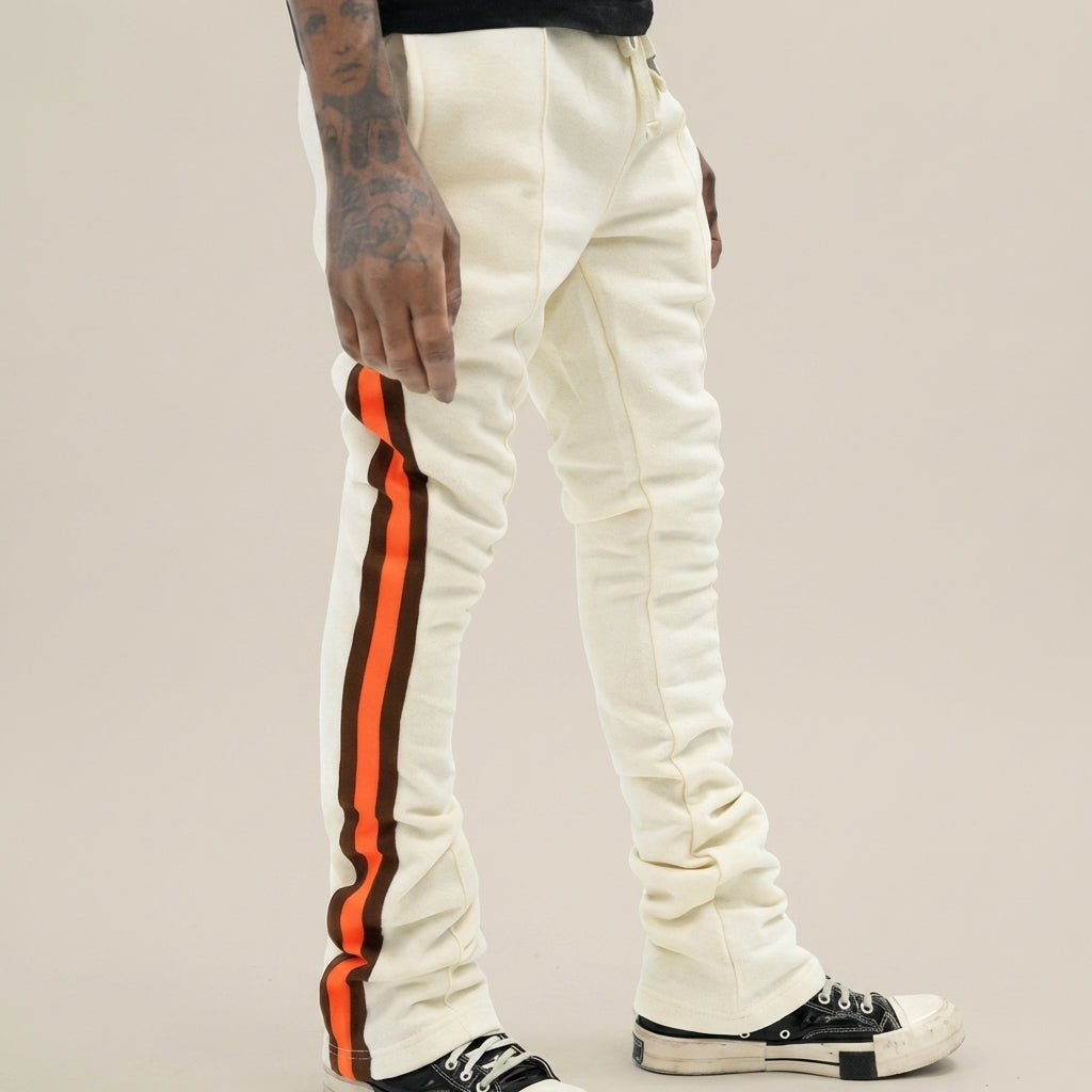 Urban Flare joggers in cream with orange and brown side stripes, worn by a person with tattoos, against a neutral background.