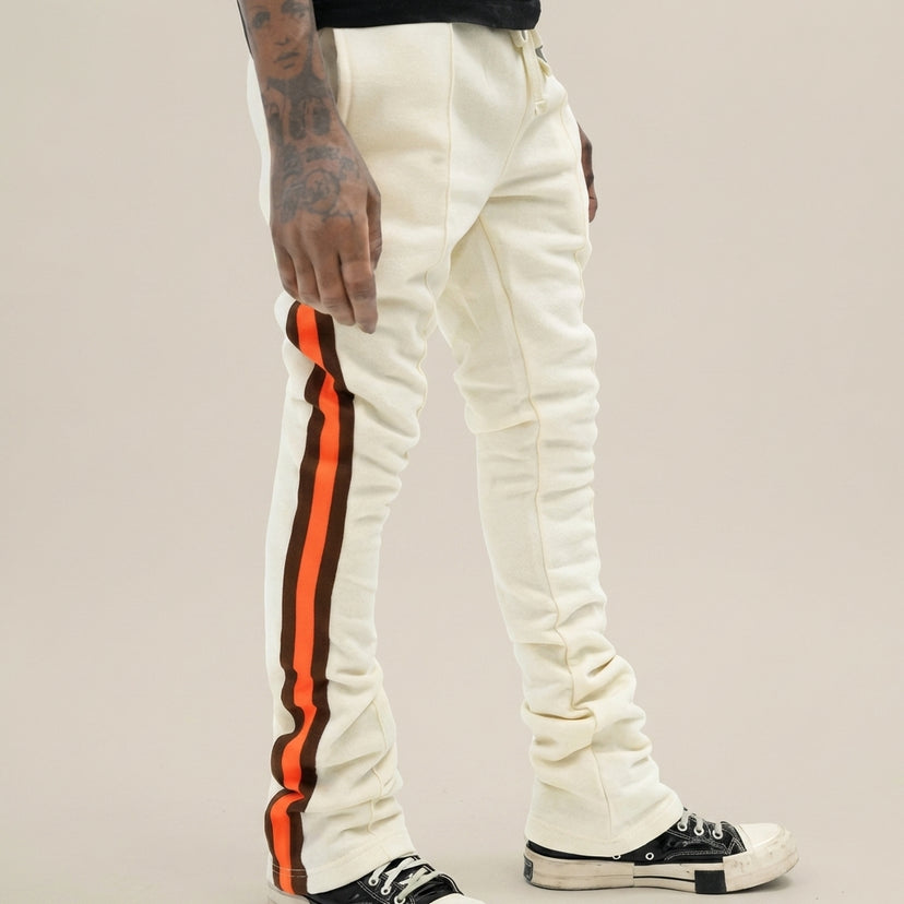 Urban Flare joggers in cream with orange and brown side stripes, worn by a person with tattoos, against a neutral background.