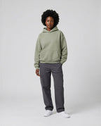 Blank heavyweight oversized hoodie in olive green, worn with gray cargo pants and white sneakers, standing against a neutr...