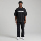 Black LEGENDARY T-shirt with white text, worn by a model standing against a neutral background, paired with dark pants.