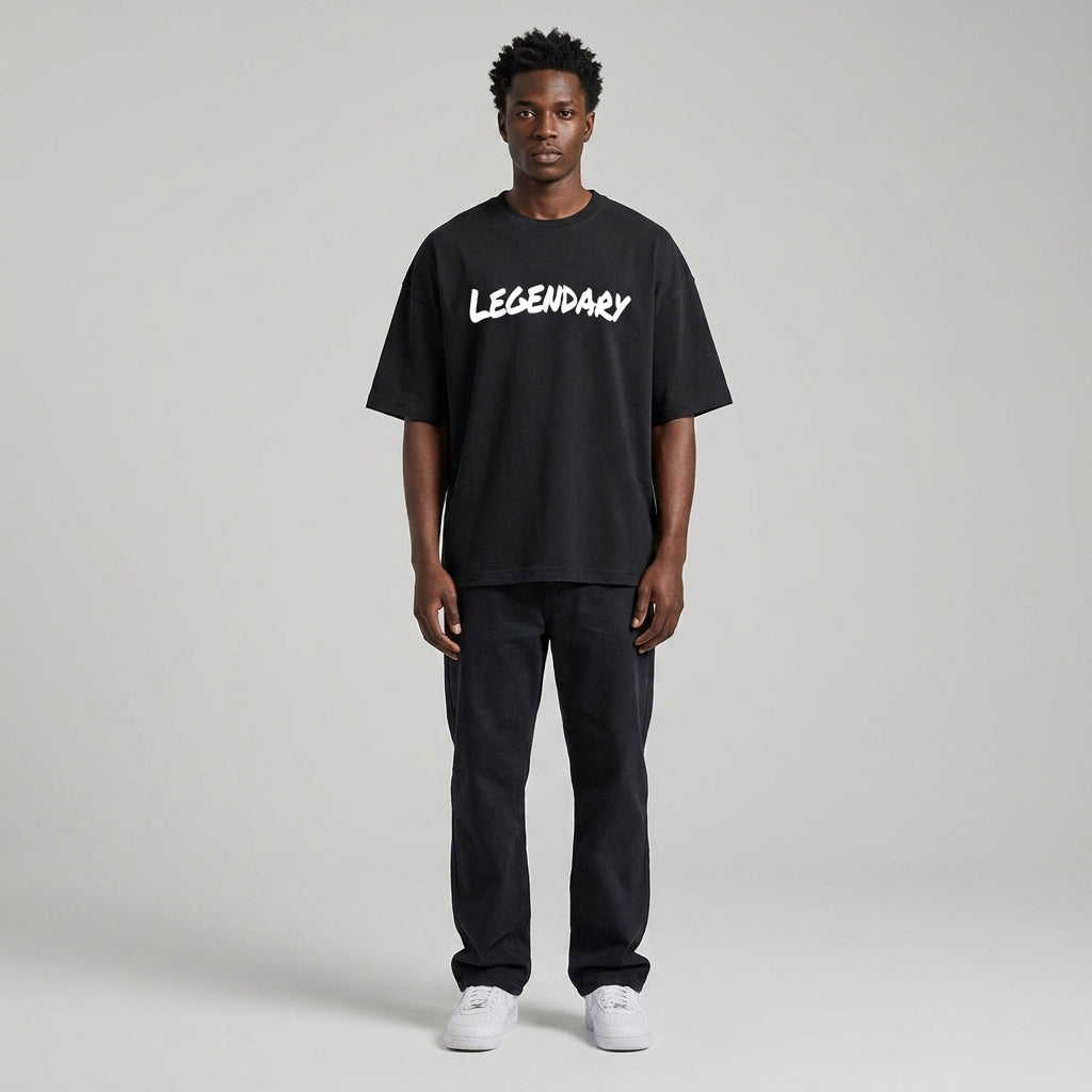 Black LEGENDARY T-shirt with white text, worn by a model standing against a neutral background, paired with dark pants.