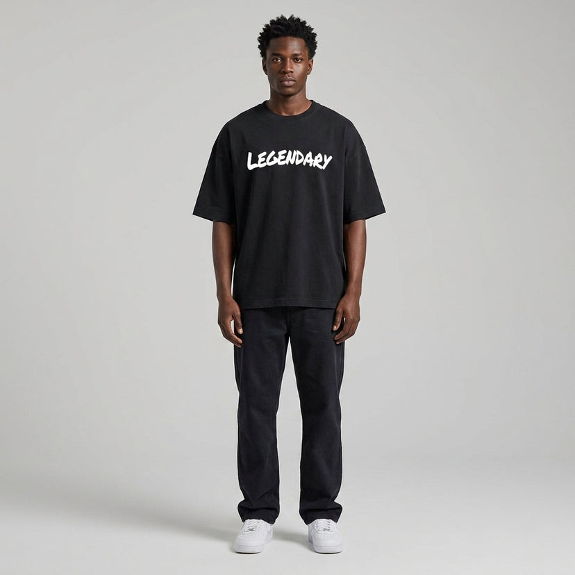Black LEGENDARY T-shirt with white text, worn by a model standing against a neutral background, paired with dark pants.