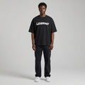 Black LEGENDARY T-shirt with white text, worn by a model standing against a neutral background, paired with dark pants.