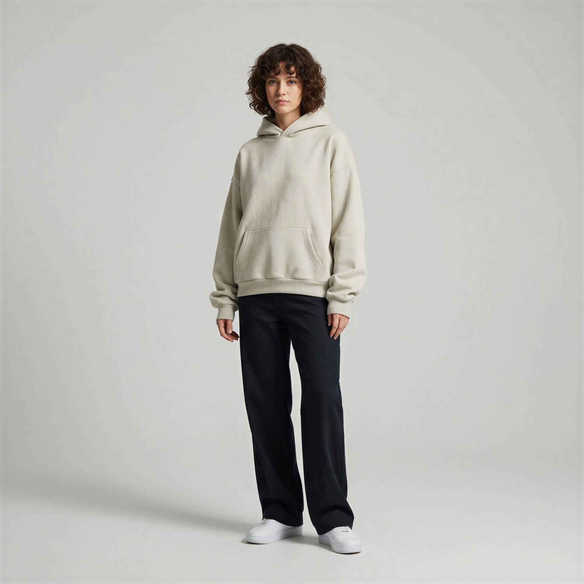 Blank heavyweight oversized hoodie in light beige, worn by a model with curly hair, paired with black pants.